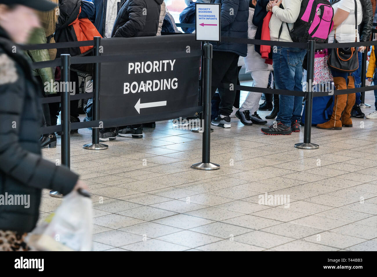 Anonymous passengers in queue behind PRIORITY BOARDING sign at the