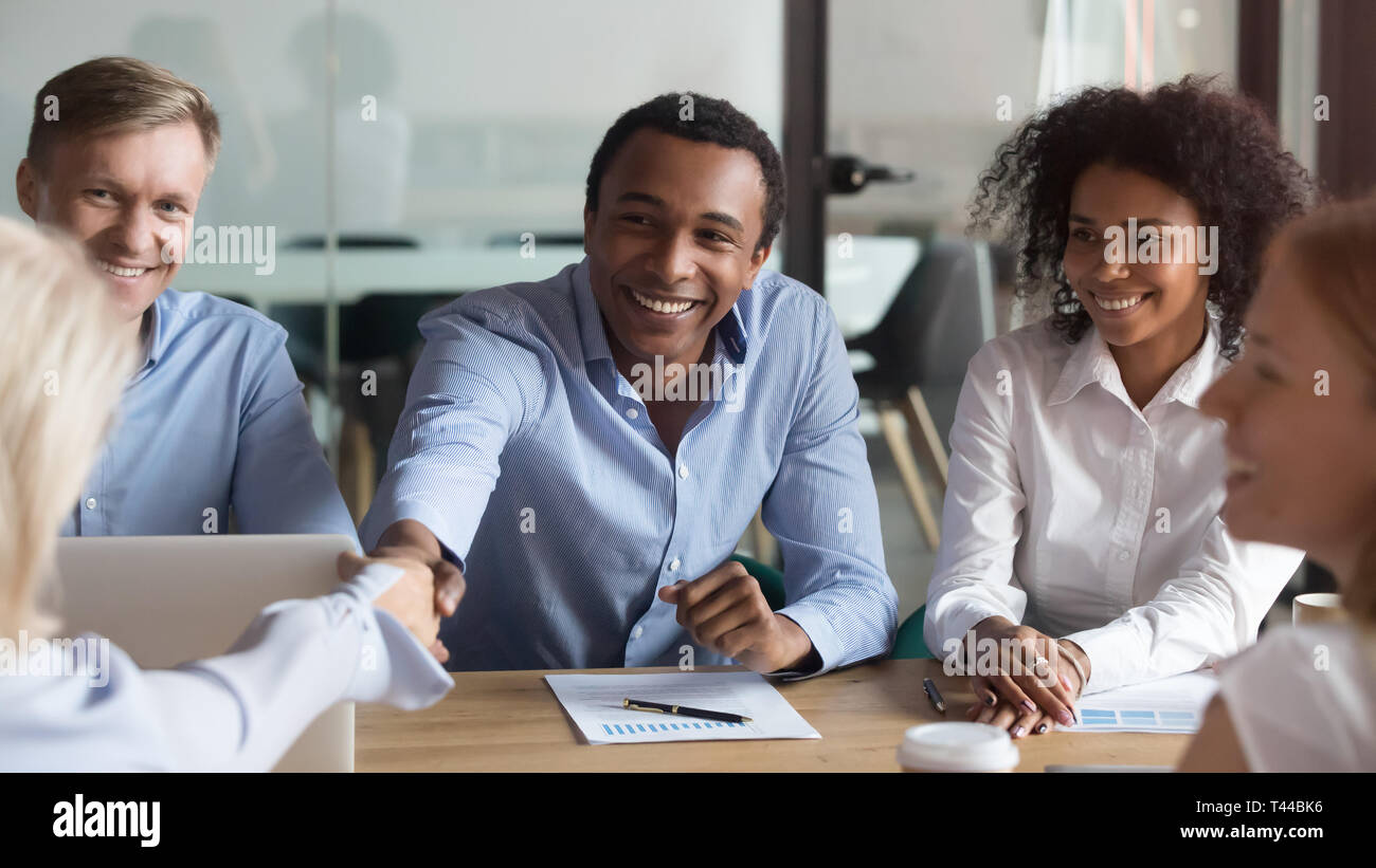 Smiling african manager handshaking greeting caucasian client at group ...