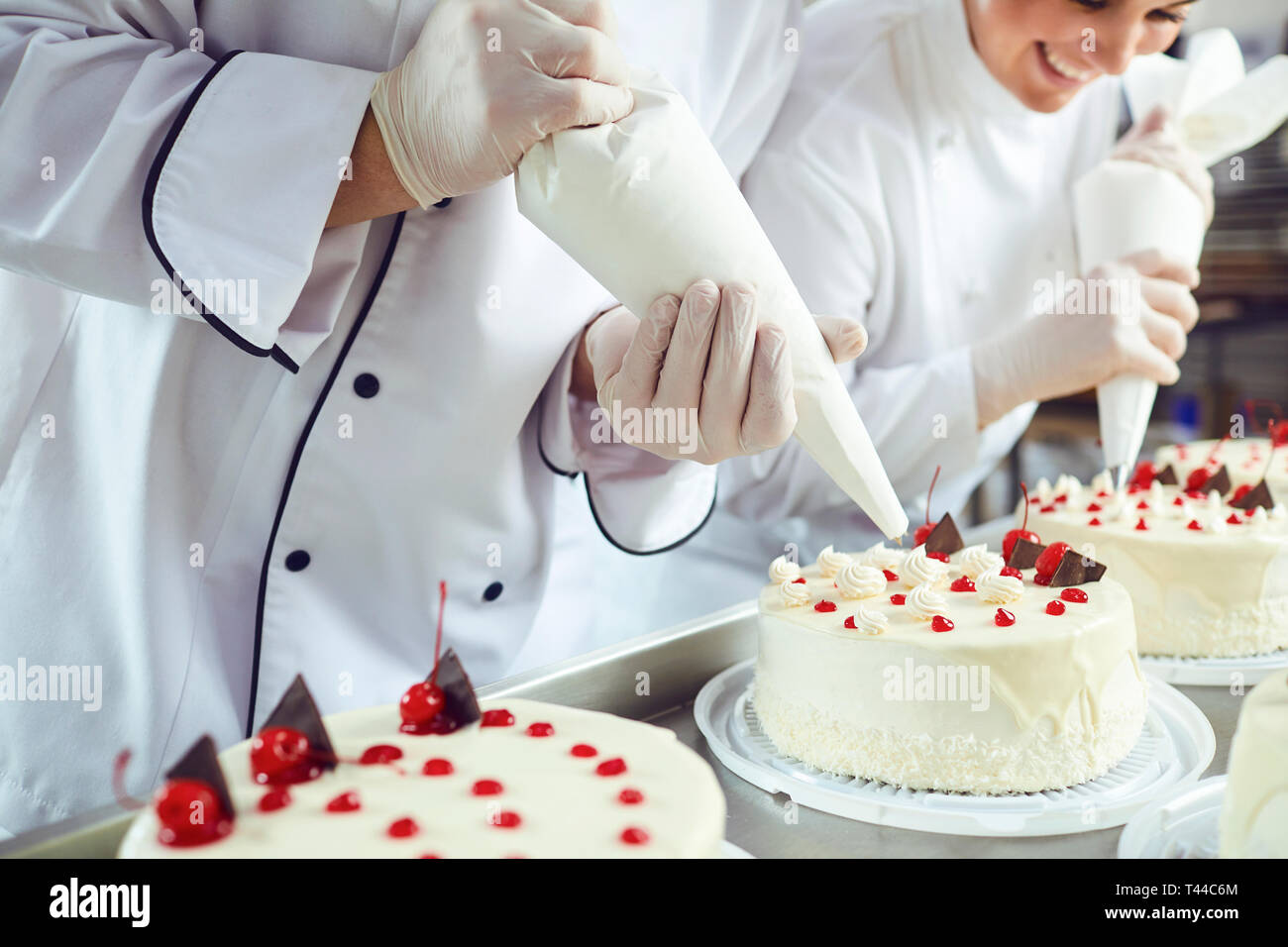 Two pastry chefs decorate a cake from a bag in a pastry shop Stock