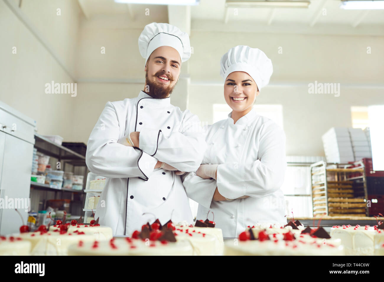Pastry chefs in white uniform are smiling at bakery. Stock Photo