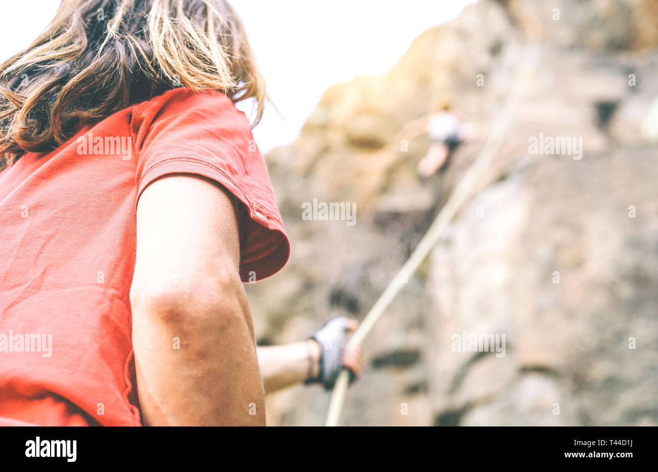 Woman climbing up on mountain cliff while man helping her to climb to the top holding the rope - Climber in action on the rock near the peak Stock Photo
