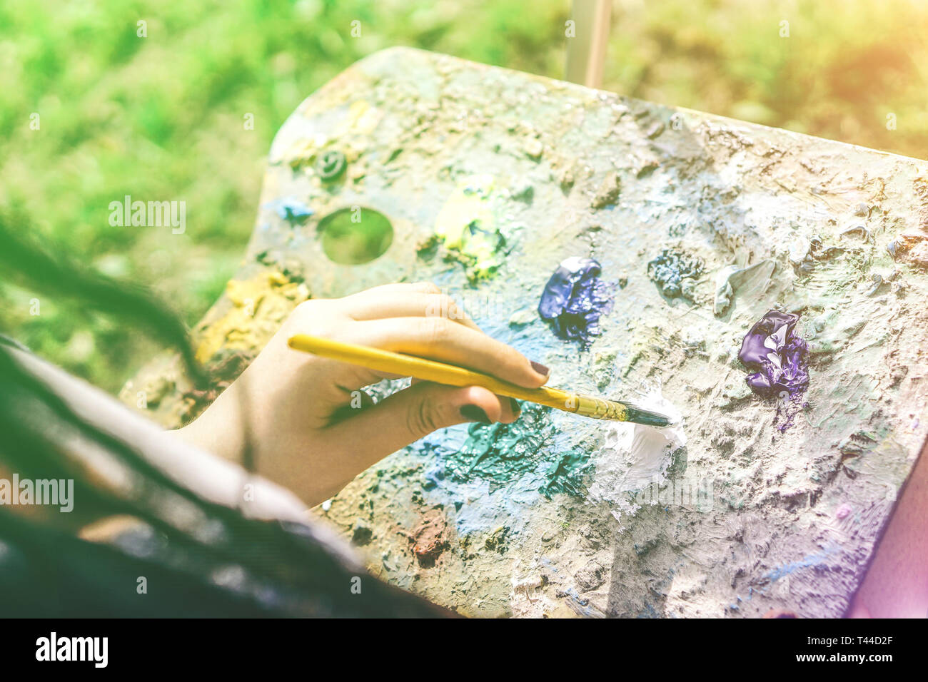 Young artist painting in a park outdoor - Close up of painter with dreadlocks hairstyle working on her art in a colorful garden Stock Photo