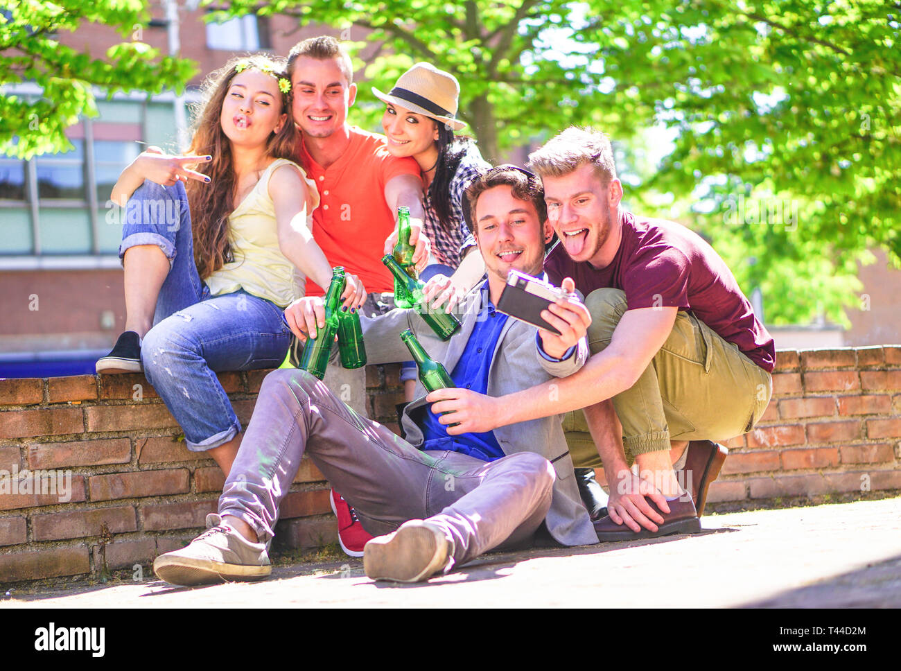 Group of happy friends drinking beers and taking selfie with a vintage camera outdoor - Young people making photos while toasting and cheering bottles Stock Photo