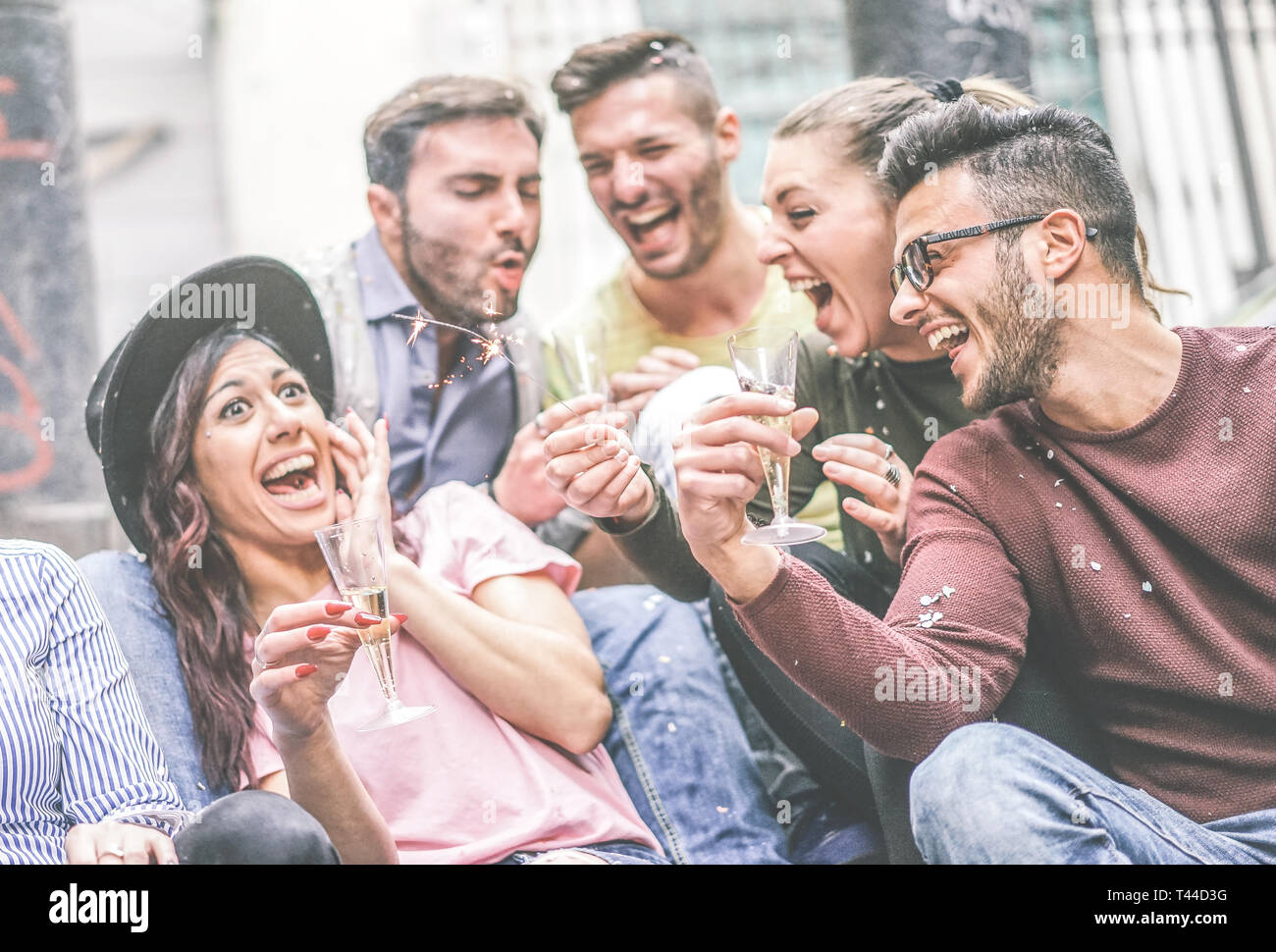 Group of happy friends making party drinking champagne while throwing confetti outdoor - Young people laughing and having fun celebrating holidays Stock Photo