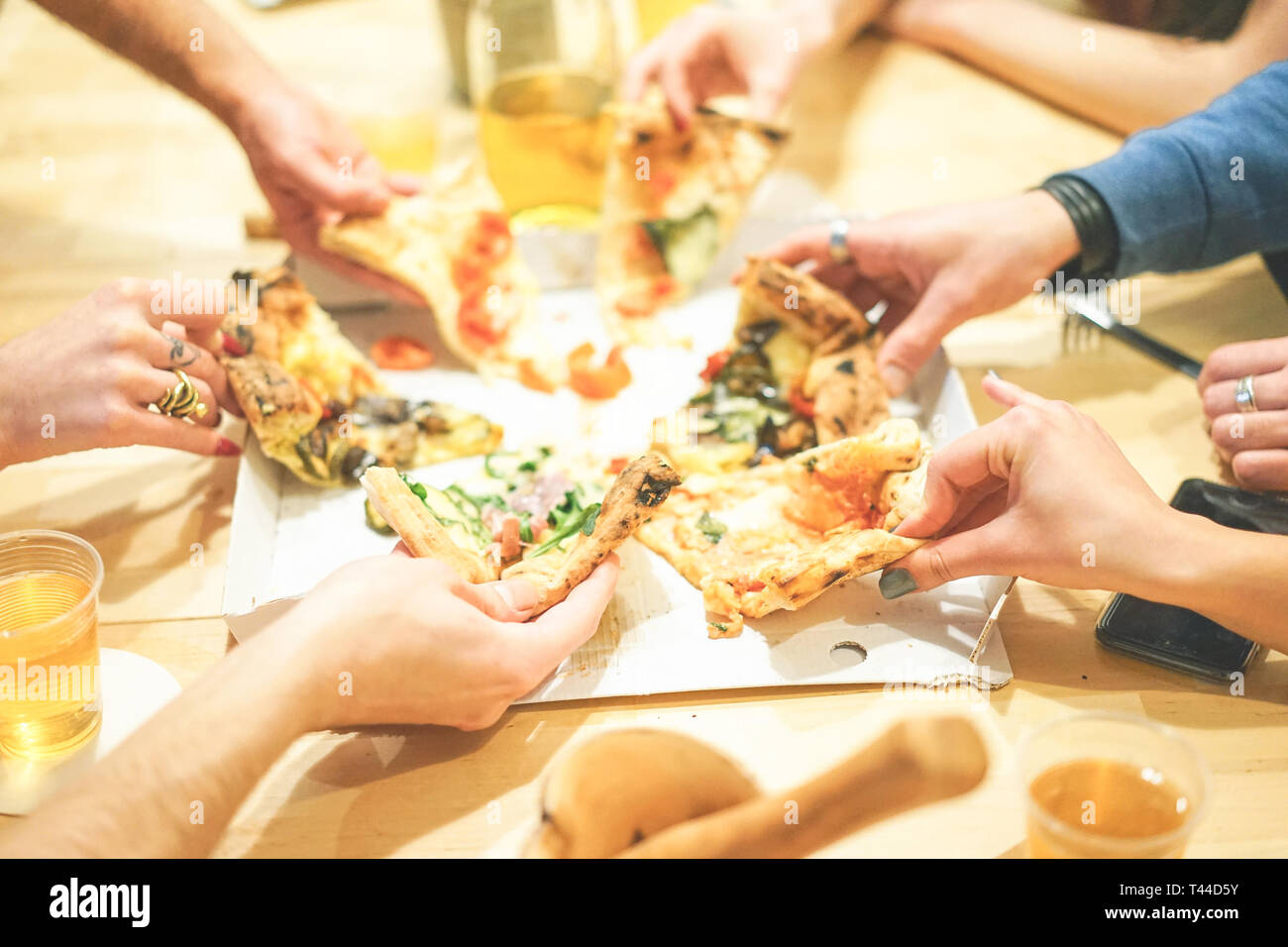 Close up of people hands taking diverse slices of delicious italian pizza at home - Group of friends enjoying a meal eating take away food Stock Photo