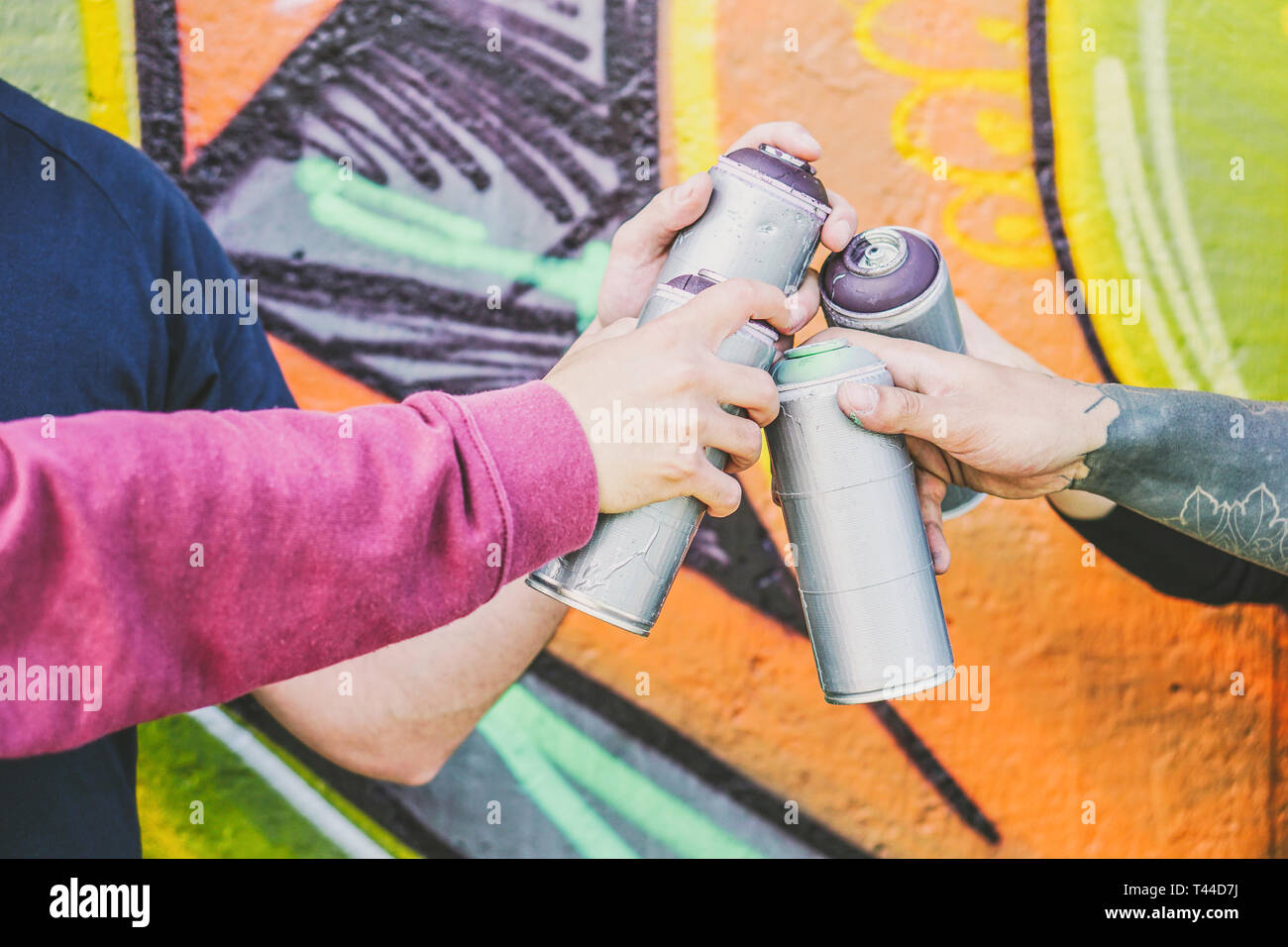 Close up hands of people holding color spray cans against the graffiti wall - Graffiti artists at work - Rebels, lifestyle, street art concept Stock Photo