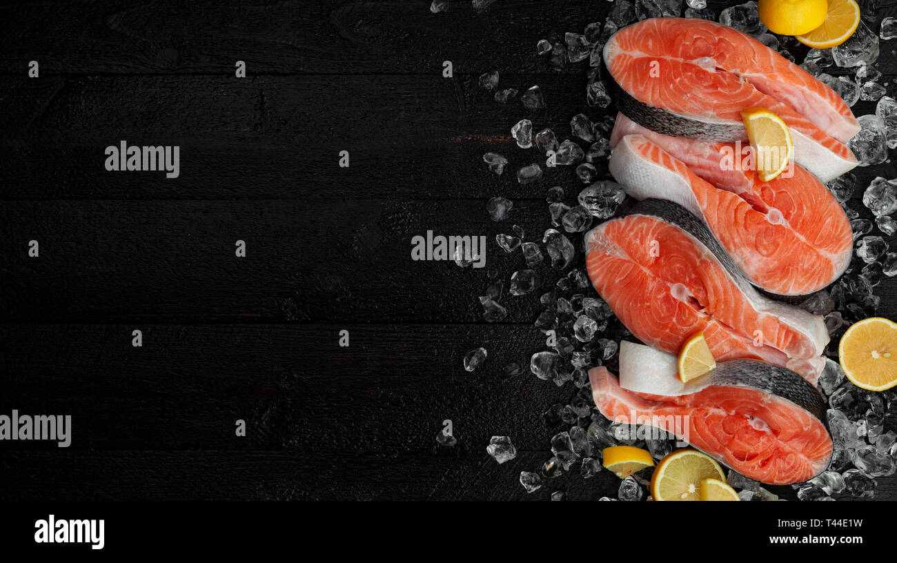 Fresh salmon steaks on black background, piece of chilled red fish on ice, top view Stock Photo