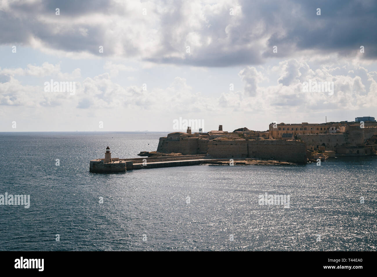View of the Grand Harbour entrance and old medieval Ricasoli East Breakwater with red lighthouse and Fort Ricasoli seen from Valletta, Malta Stock Photo