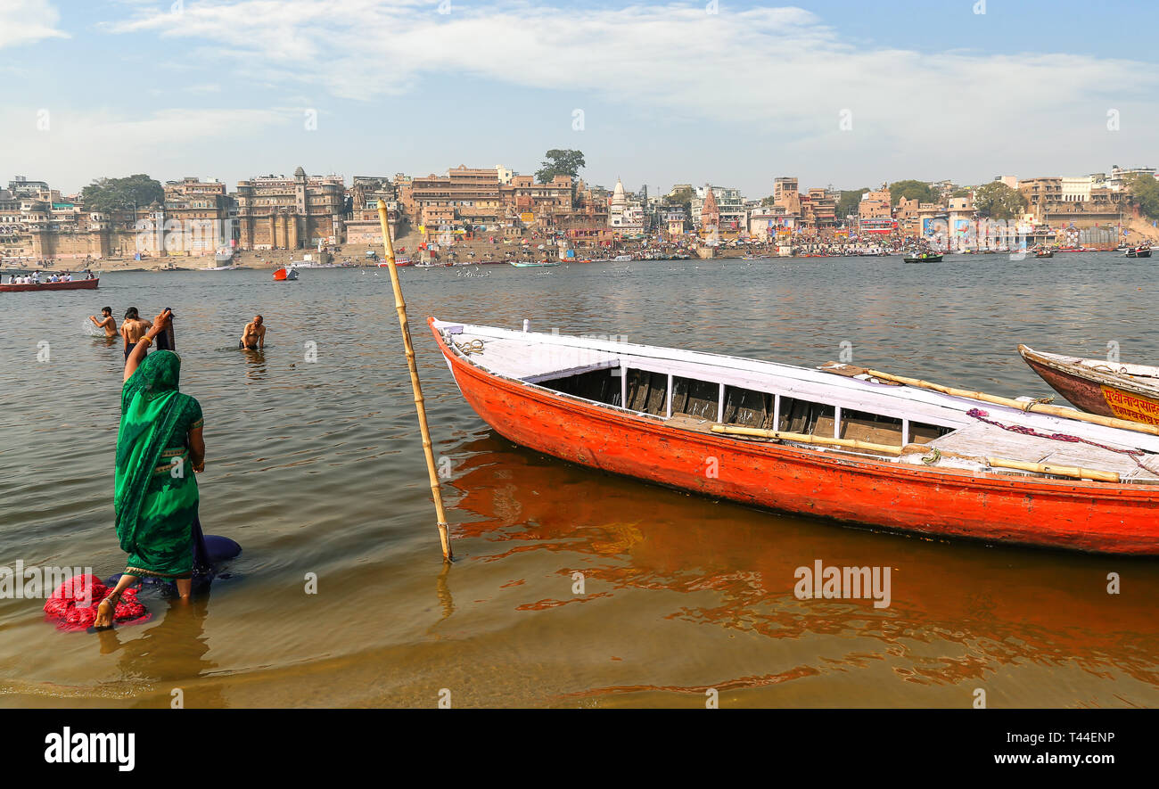 Tourists pilgrims bathing and washing clothes at the Ganges river bank overlooking ancient Varanasi ancient city architecture Stock Photo