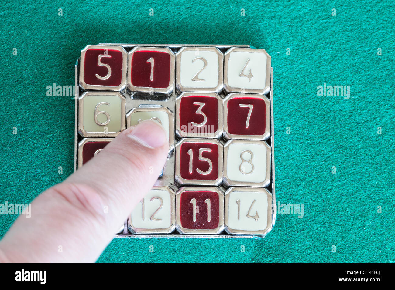 finger slides tile in 15-puzzle (magic 15) sliding puzzle game close up on green baize table Stock Photo