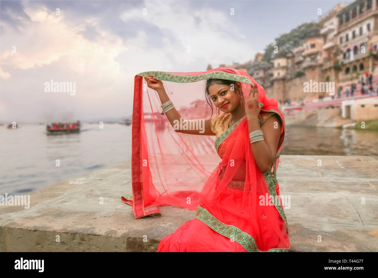 young indian girl in traditional dress saree pose for a photo overlooking the historic varanasi city architecture and ganges river ghat at twilight T44G7T
