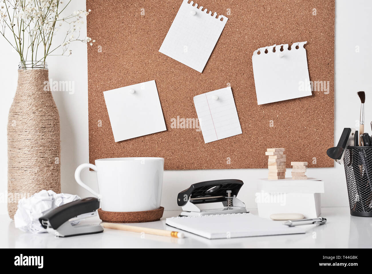 Cork board with office supplies, cup and plant in bottle vase on white