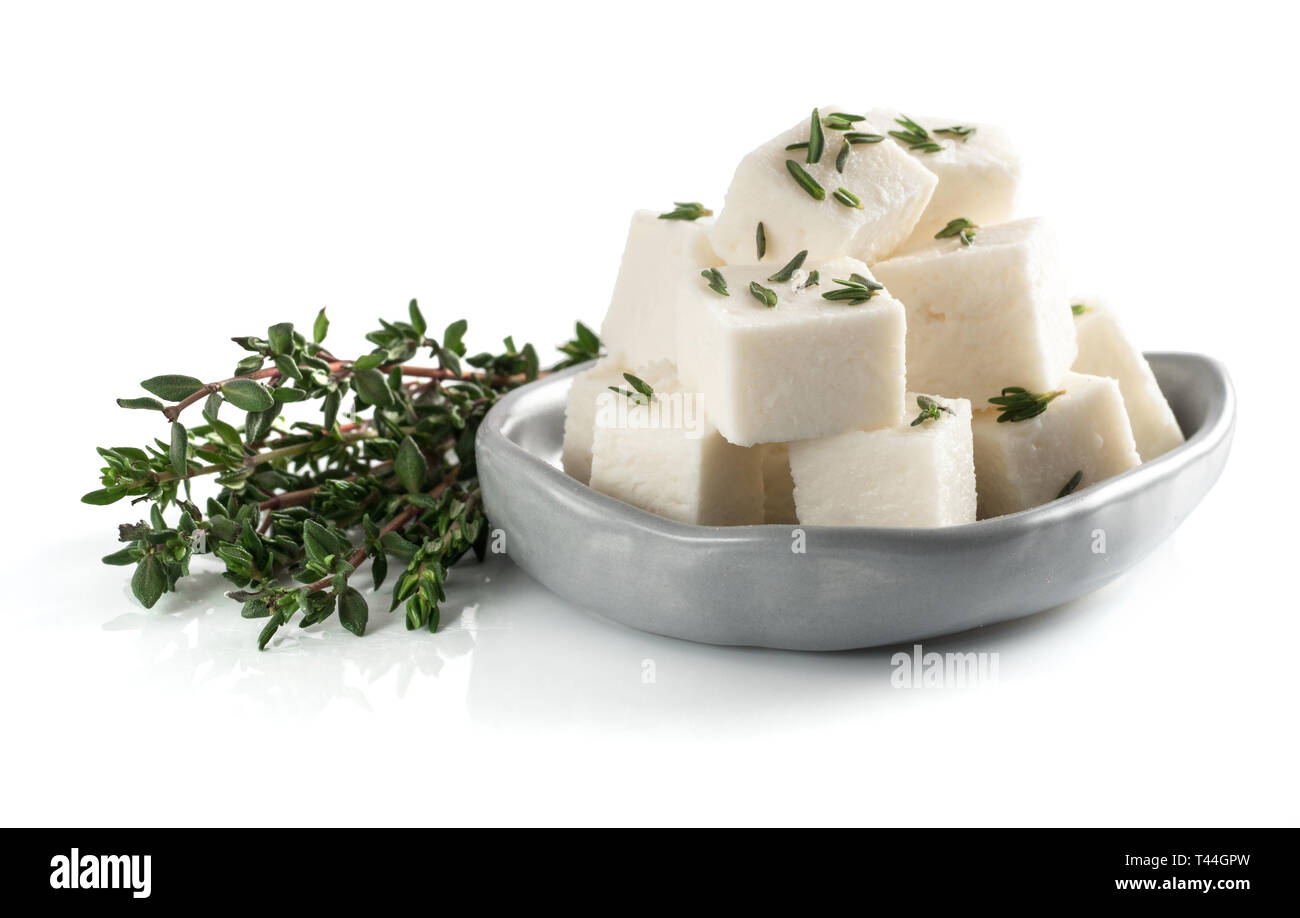 Diced soft cheese in rustic plate and fresh thyme isolated on white background with clipping path. Stock Photo