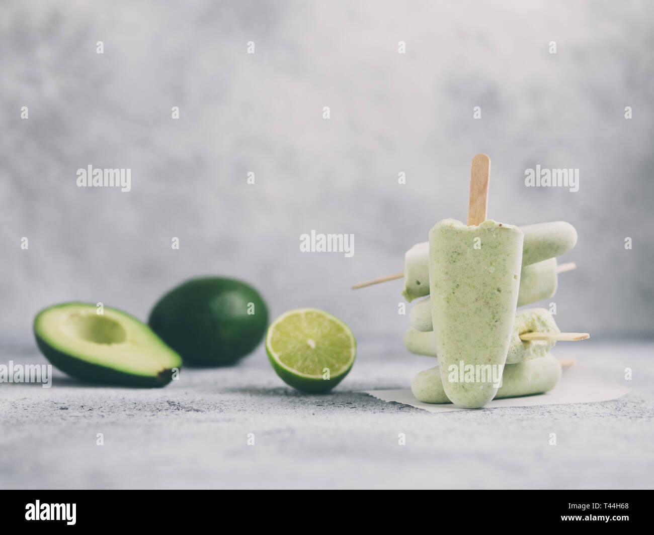 Homemade raw vegan avocado lime popsicle. Sugar-free, non-dairy green ice cream on gray cement textured background. Copy space. Ideas and recipes for healthy snack, dessert or smoothie Stock Photo