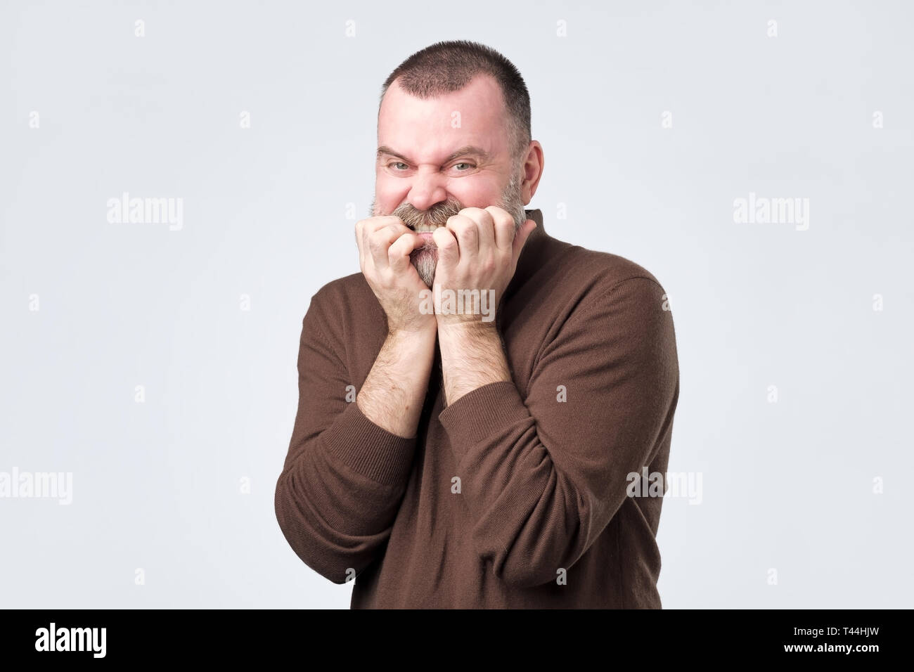 Man with beard in brown shirt biting nails in fear Stock Photo