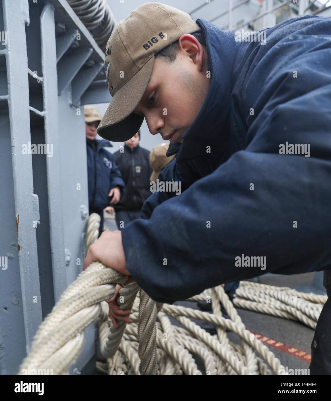 NORFOLK, Va. (Feb. 20, 2019) Seaman Matthew Luera helps fake down mooring lines during a sea and anchor evolution on the fantail aboard the amphibious assault ship USS Bataan (LHD 5). The ship is underway conducting sea trials. Stock Photo