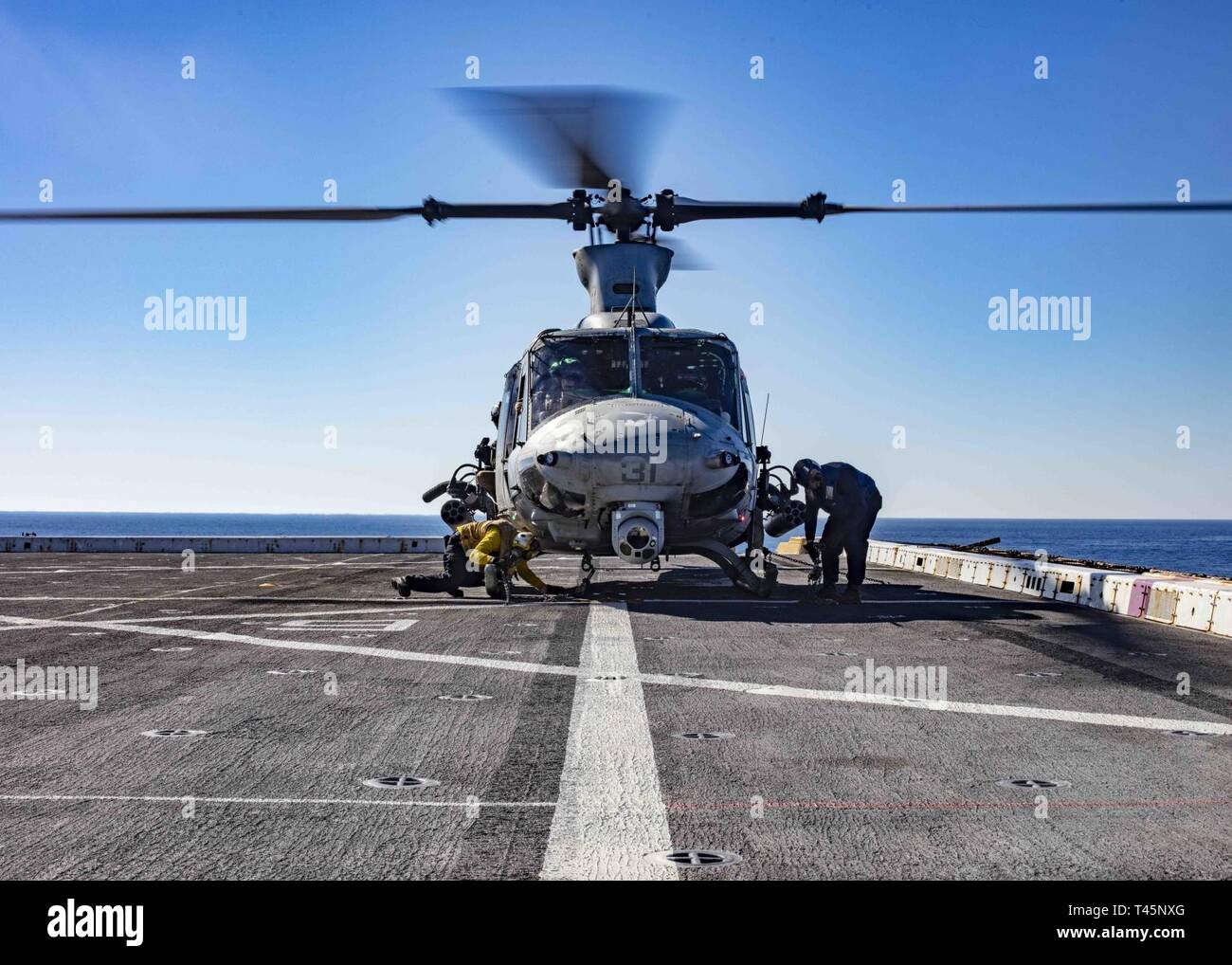 MEDITERRANEAN SEA (Mar. 5, 2019) Sailors secure a UH-1Y Huey helicopter assigned to the “Black Knights” of Marine Medium Tiltrotor Squadron (VMM) 264 (Reinforced) to the flight deck of the San Antonio-class amphibious transport dock ship USS Arlington (LPD 24), Mar. 5, 2019. Arlington is on a scheduled deployment as part of the Kearsarge Amphibious Ready Group in support of maritime security operations, crisis response and theater security cooperation, while also providing a forward naval presence. Stock Photo