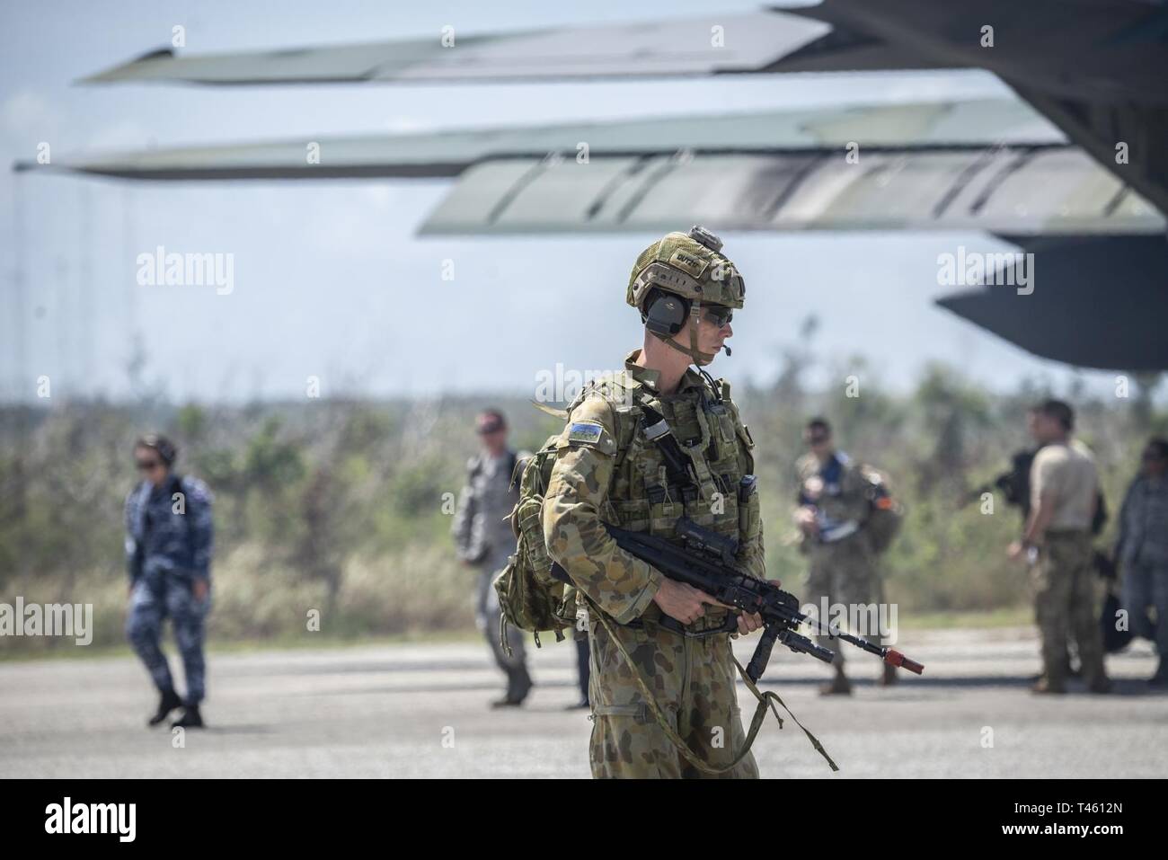 A Royal Australian Air Force member provides security for passengers exiting a plane at Tinian, U.S. Commonwealth of the Northern Marianas Islands stands during exercise Cope North Feb. 19, 2019. Cope North is an annual multilateral U.S. Pacific Air Forces-sponsored field training exercise focused on combat air forces large-force employment and mobility air forces humanitarian assistance and disaster relief training to enhance interoperability among U.S., Australian and Japanese forces. Stock Photo