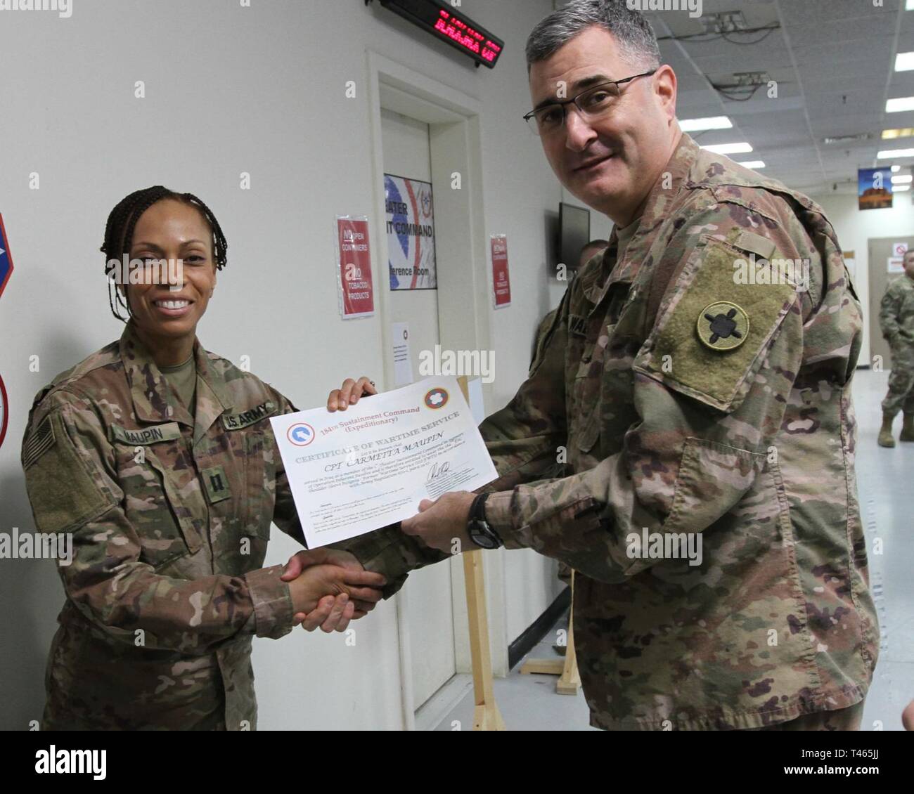 Brig. Gen. Clint E. Walker, commanding general of the 184th Sustainment Command, presents a certificate of wartime service to Cpt. carmetta Maupin following the placement of the 184th ESC patch on his right shoulder at Camp Arifjan, Kuwait, Mar. 3, 2019. Stock Photo