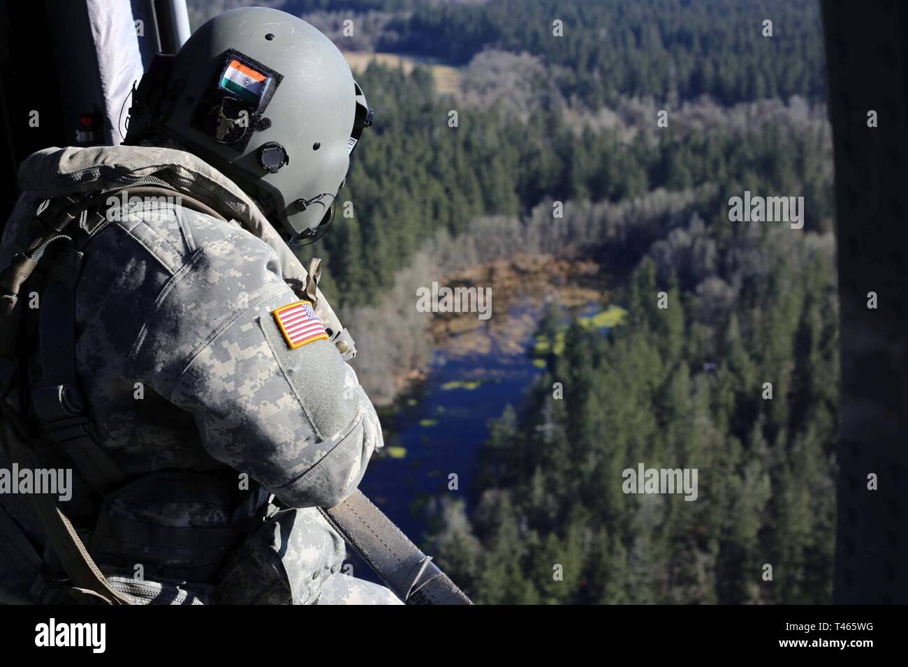 A crew chief on a Blackhawk helicopter watches the placement of a water bucket pendent and relays its information to the pilots during a check ride with the US Forest Service. Washington National Guard aviators conduct water bucket training annually in preparation for wild land fire response. Stock Photo