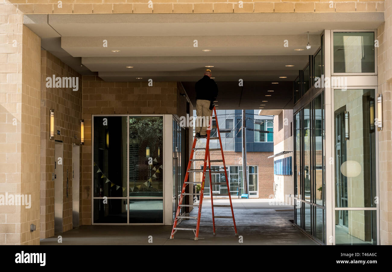 Worker on ladder changing light bulb outside commercial building Stock Photo