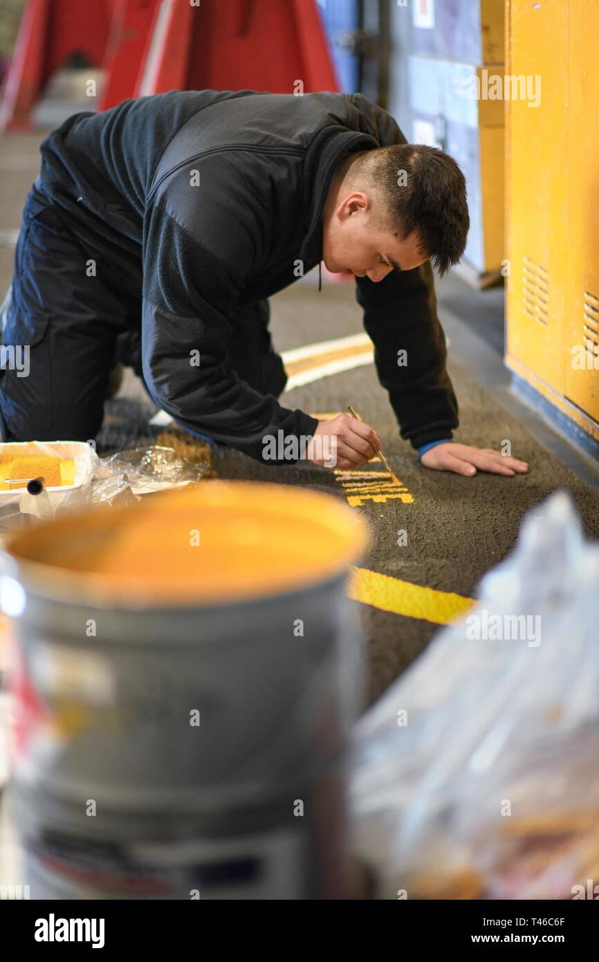 PACIFIC OCEAN (March 12, 2019) Aviation Boatswain’s Mate (Handling) 3rd Class David Deleon, from Guam, stencils the words “fire lane” on the non-skid in the hangar bay of the aircraft carrier USS Theodore Roosevelt (CVN 71). Theodore Roosevelt is conducting routine operations in the Eastern Pacific. Stock Photo