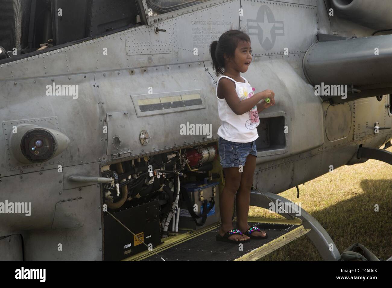 A young Tinian resident stands for a photo beside an AH-1Z Viper helicopter on Tinian, Commonwealth of the Northern Mariana Islands, March 11, 2019. Marines and Sailors with Combat Logistics Battalion 31 led a multi-service task force, partnering with the Federal Emergency Management Agency, to help the U.S. citizens of Tinian begin recovery efforts in the wake of Super Typhoon Yutu last year. The Marines and Sailors, currently participating in two weeks of unit-level training on nearby Guam, visited Tinian to meet with members of the community affected by Yutu in late October 2018. CLB-31 pro Stock Photo