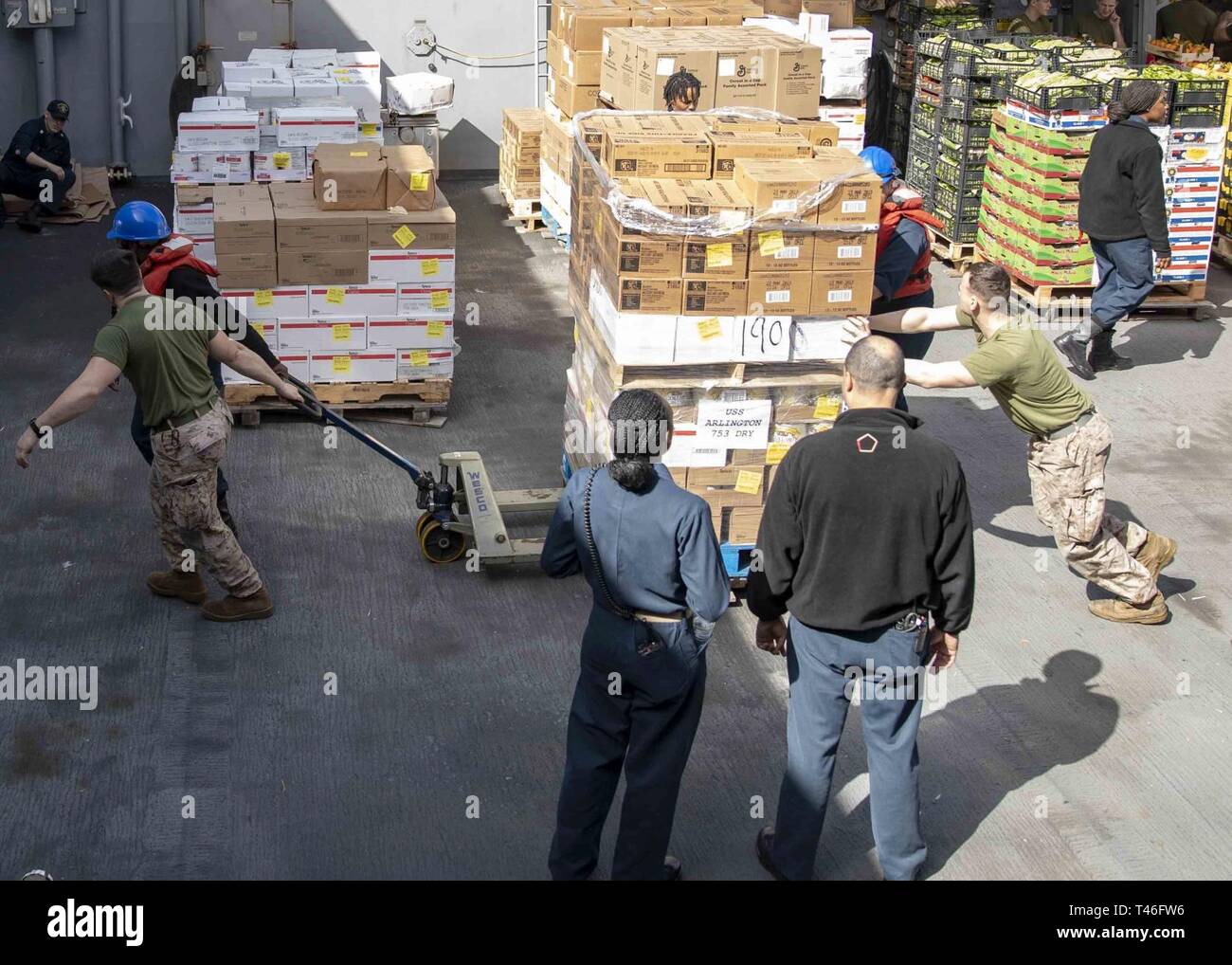 MEDITERRANEAN SEA (Mar. 9, 2019) - U.S. Marines and Sailors with the 22nd Marine Expeditionary Unit and the San Antonio-class amphibious transport dock ship USS Arlington (LPD-24) help each other move pallets of stores across the boat valley of the Arlington during a replenishment-at-sea, Mar. 9, 2019. The USS Arlington is making a scheduled deployment as part of the 22nd MEU and the Kearsarge Amphibious Ready Group, in support of maritime security operations, crisis response and theater security cooperation, while also providing a forward Naval and Marine presence. Stock Photo