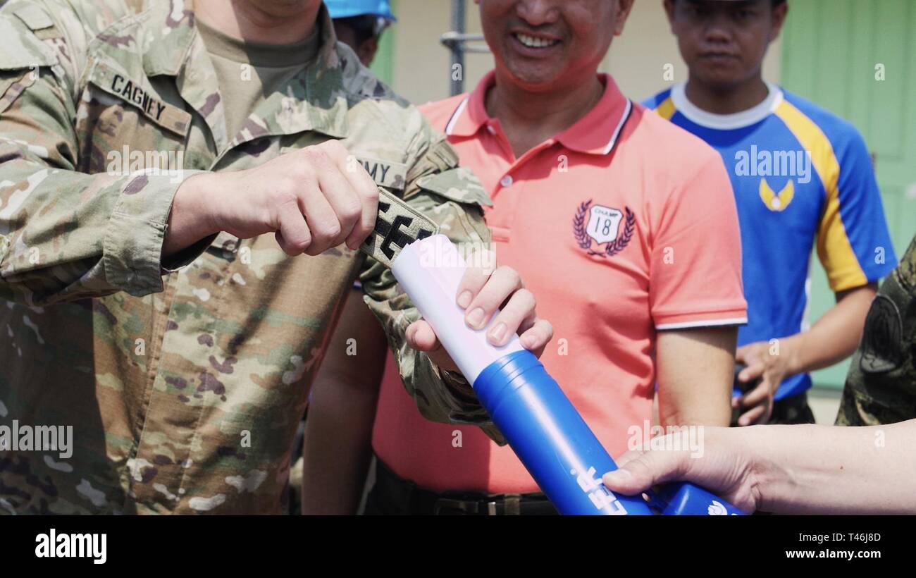 U.S. Army 1st Lt. Brendon Cagney, Engineering Civic Action Project (ENCAP) 4 officer in charge, places a 130th Engineer Brigade patch into the time capsule during the emplacement of the capsule at the ENCAP 4 opening ceremony as part of Exercise Balikatan, March 12, 2019.  Mr. Francisco Bautista, Department of Education district supervisor and an airman from the 355th Aviation Engineer Wing, Armed Forces of the Philippines, observes.  The military relationship between the U.S. and Philippines is strong and based on mutual respect and cooperation.  Exercise Balikatan, in its 35th iteration, is  Stock Photo
