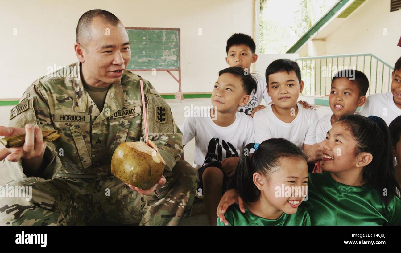 U.S. Army Sgt. Kyle Horiuchi, 561st Engineer Construction Company, 84th Engineer Battalion, 130th Engineer Brigade, 8th Theater Sustainment Command, visits with local children during a catered lunch at the Engineering Civic Action Project 4 opening ceremony as part of Exercise Balikatan, March 12, 2019. Exercise Balikatan, in its 35th iteration, is an annual U.S.-Philippine military training exercise focused on a variety of missions, including humanitarian assistance and disaster relief, counterterrorism, and other combined military operations. The military relationship between the U.S. and th Stock Photo