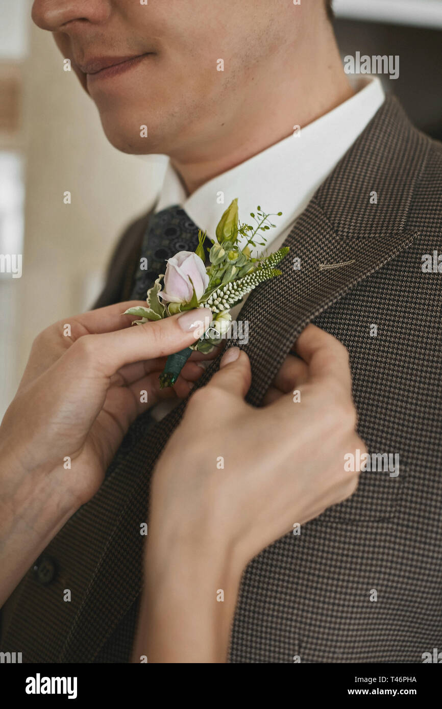 Female hands put on fresh boutonniere on the jacket of a young handsome man Stock Photo