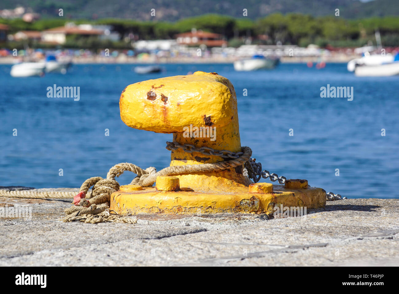 A mooring bollard entwined with a mooring rope. Moored ships at the port quay Stock Photo