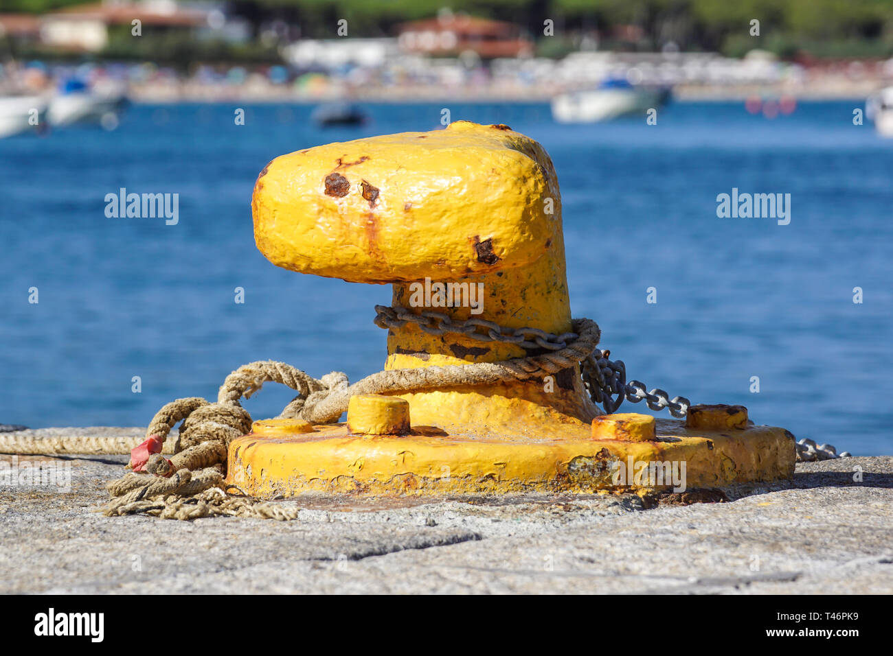 A mooring bollard entwined with a mooring rope. Moored ships at the port quay Stock Photo
