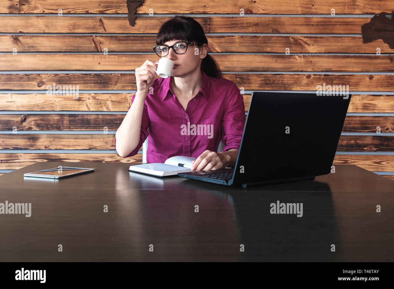 Businesswoman concentrating on her work while drinking a cup of coffee typing on her laptop computer with a serious expression Stock Photo