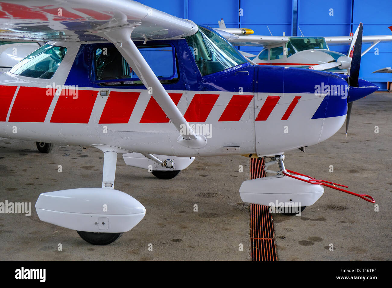 Small sport aircraft in hangar, side view, white, blue and red fuselage Stock Photo