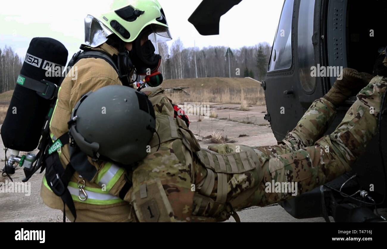 A Latvian soldier drags a simulated casualty who is a U.S. Soldier with Company A, 3rd Assault Helicopter Battalion, 1st Aviation Regiment, 1st Combat Aviation Brigade, 1st Infantry Division from a UH-60 Blackhawk during a mass casualty training for exercise Ready To Fight, March 14, at Lielvarde Air Base, Latvia. Ready To Fight is a multinational exercise which demonstrates the collective defense achieved as the U.S. skillfully works together with ally and partner nations. Participation in multinational exercises like RTF develops professional relationships and improves overall coordination w Stock Photo