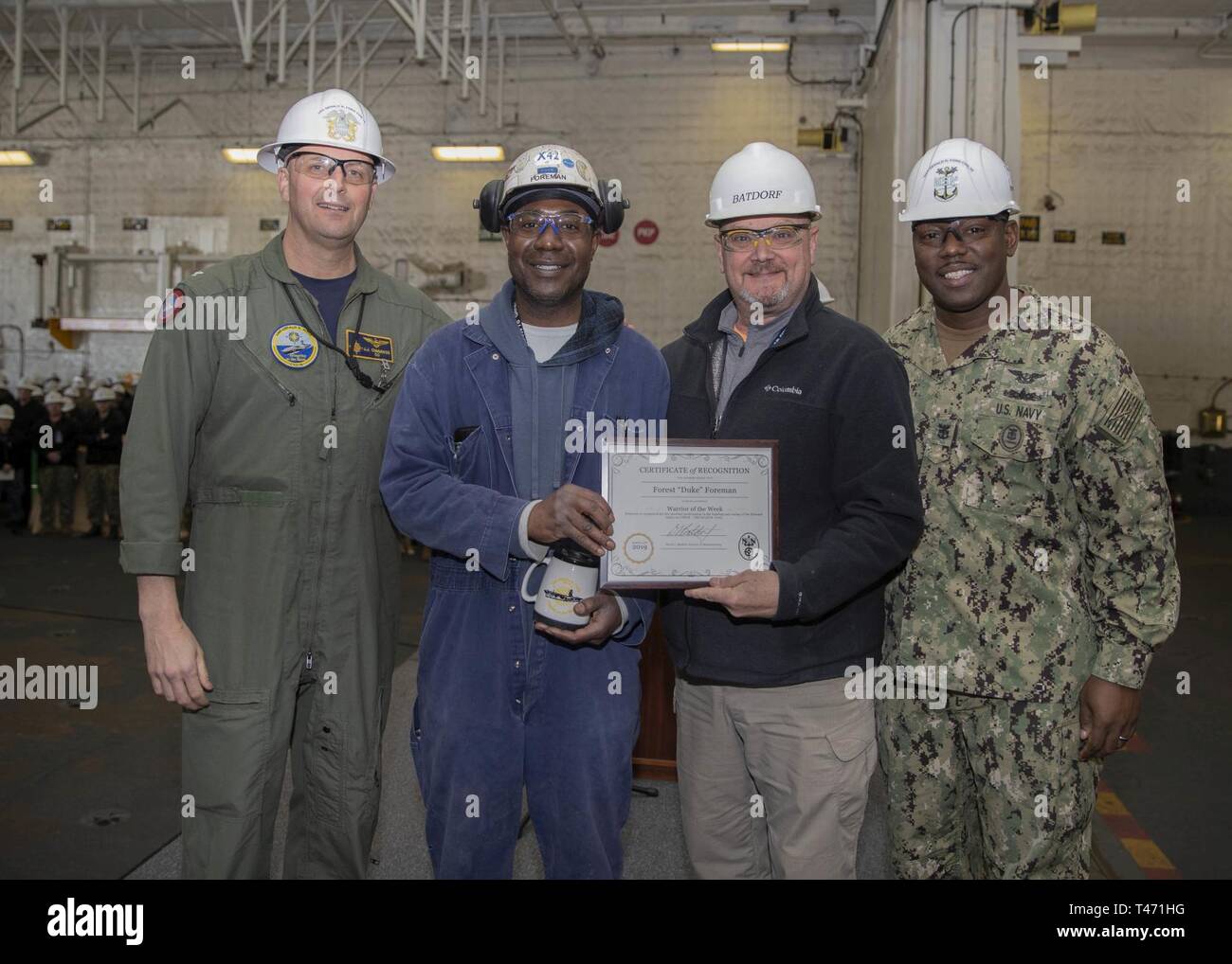 NEWPORT NEWS, Va. (March 14, 2019) Huntington Ingalls Industries-Newport News Shipbuilding employee Forest Foreman receives the Warrior of the Week award for outstanding performance from Capt. John J. Cummings, Ford's commanding officer, Command Master Chief De’Andre Beaufort and Mr. Dave Batdorf, CVN 78 Construction Supervisor during an all-hands call in the ship's hangar bay. Ford is currently undergoing its post-shakedown availability at Huntington Ingalls Industries-Newport News Shipbuilding. Stock Photo