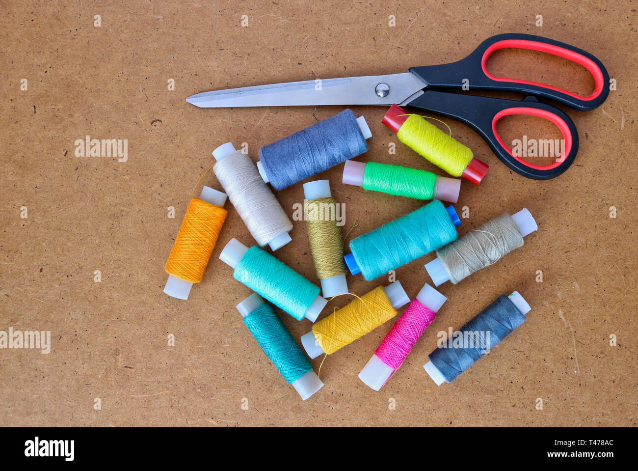 Multicolor sewing threads on a roll for sewing and tailoring scissors on a wooden background. With copy space Stock Photo
