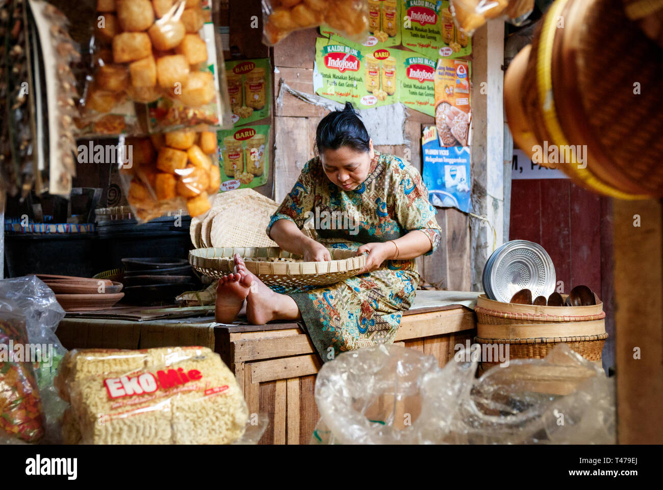 Indoor market with a local woman with a wicker basket sitting on a bench, sorting beans by hand. Borobudur Villaga, Java, Indonesia. Stock Photo