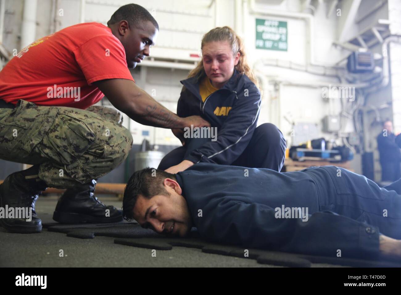 OCEAN (Mar. 15, 2019) Master-at-Arms 2nd Class Trayvond Strickland instructs Seaman Georgia Knight, as she performs a mock take down of Master-at-Arms 2nd Class John Roldan, during an oleoresin capsicum (OC) course aboard the multipurpose amphibious assault ship USS Bataan (LHD 5) The ship is underway conducting sea trials. Stock Photo