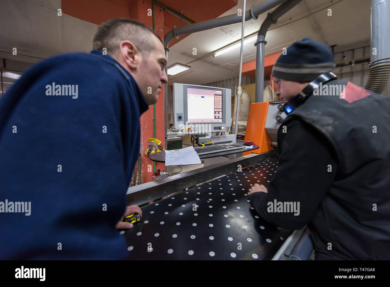 two young carpenters calculating and programming a cnc wood working machine in workshop. wood workers preparing a computer program for CNC machine at  Stock Photo