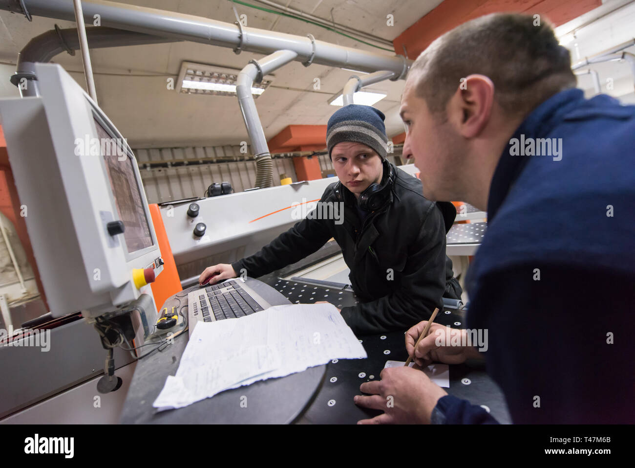 two young carpenters calculating and programming a cnc wood working machine in workshop. wood workers preparing a computer program for CNC machine at  Stock Photo