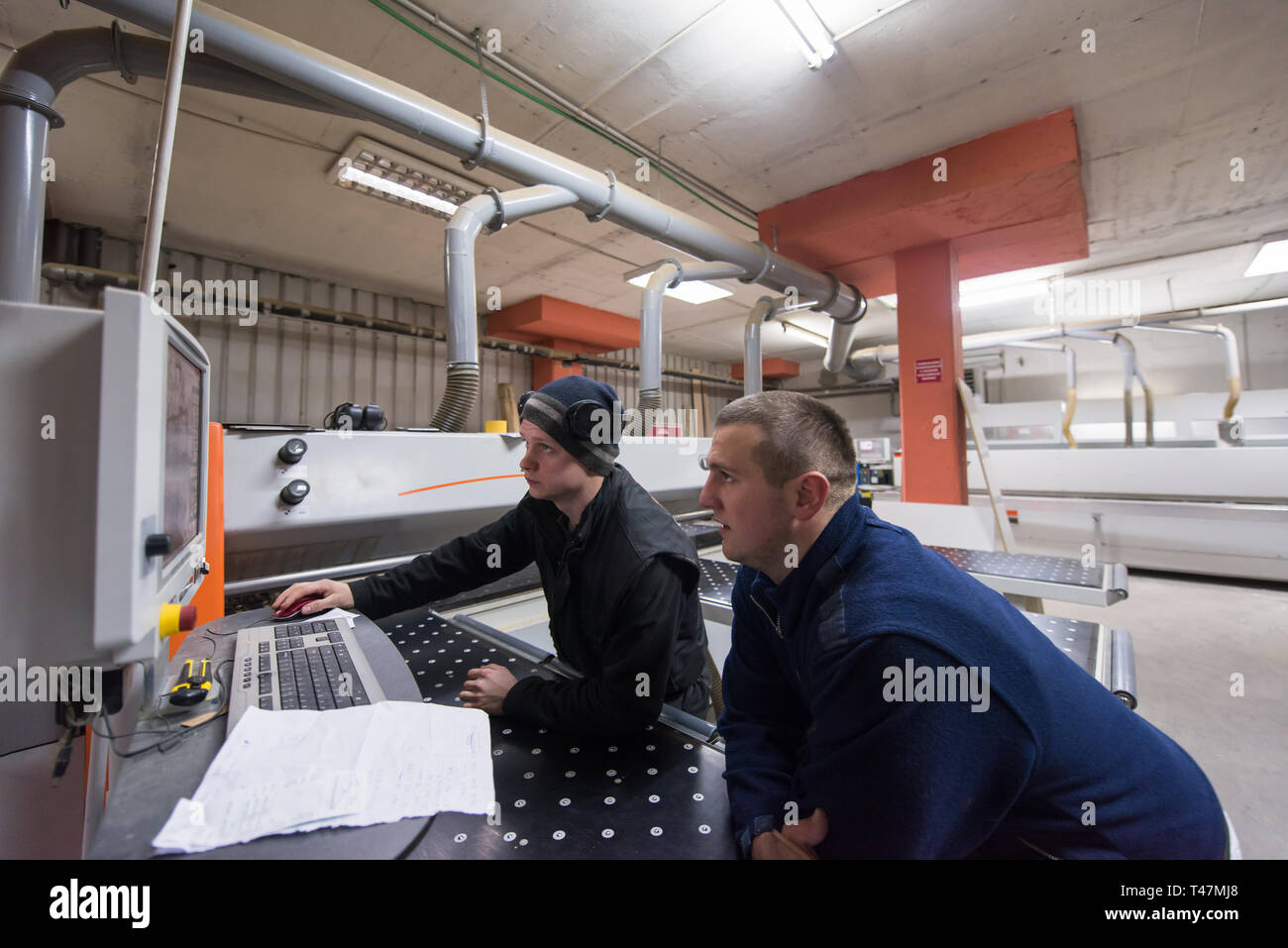 two young carpenters calculating and programming a cnc wood working machine in workshop. wood workers preparing a computer program for CNC machine at Stock Photo