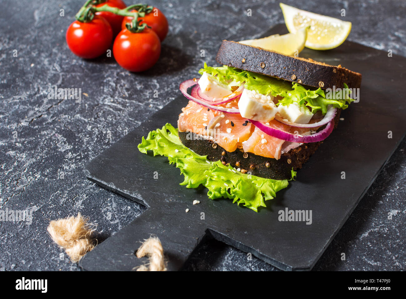 Sandwich with smoked salmon, tomato, onions and salad on black stone ...