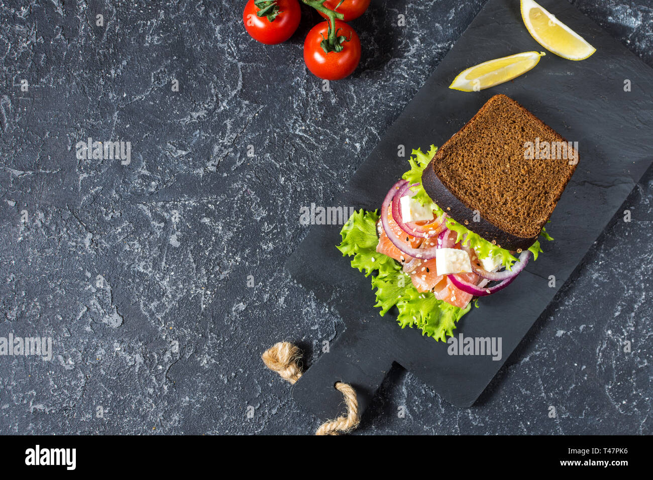 Sandwich with smoked salmon, tomato, onions and salad on black stone ...