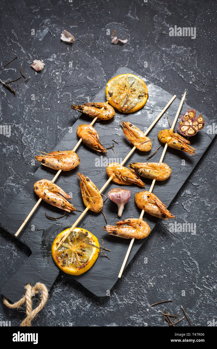 Grilled shrimp skewers with herbs, garlic and lemon on black stone background. Seafood, shelfish. Stock Photo