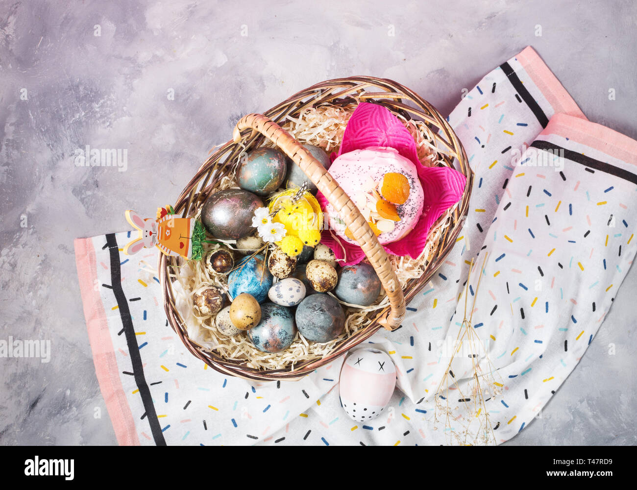 Basket with easter cakes and painted eggs on concrete background. Easter concept. Top view Stock Photo