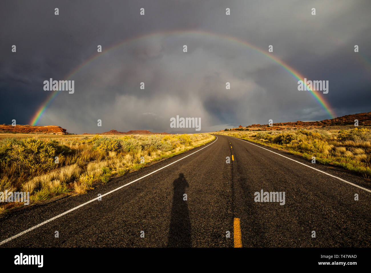 The shadow of the photographer shows on the road below a full rainbow and thuderstorm clouds over Scenic Highway 211 in Canyonlands National Park, Sou Stock Photo
