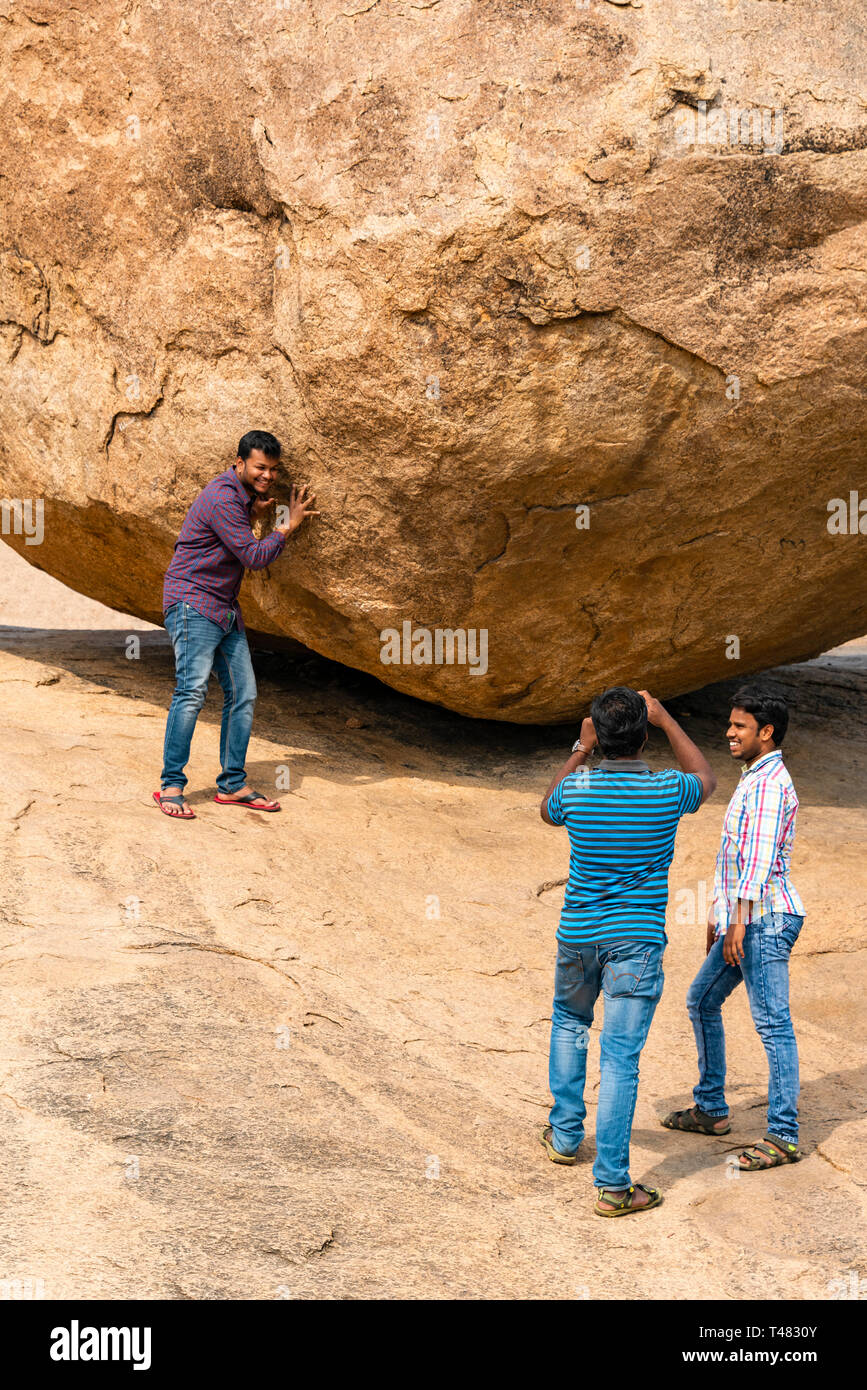 Vertical view of tourists pretending to hold up Krishna's Butterball at Mahabalipuram, India. Stock Photo