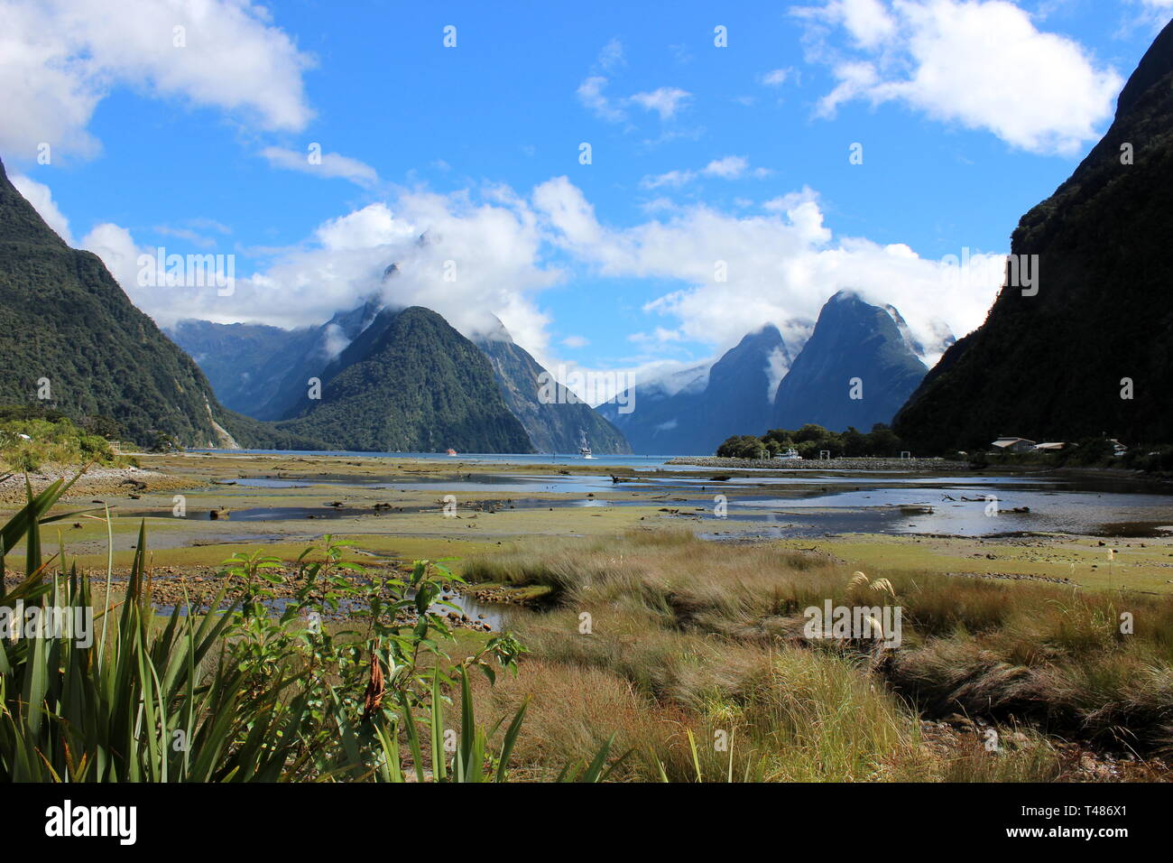 Milford Sound on a sunny day with clouds over the mountains, view from boat pier Stock Photo